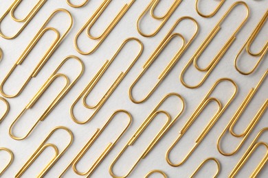 Golden paper clips on light background, flat lay