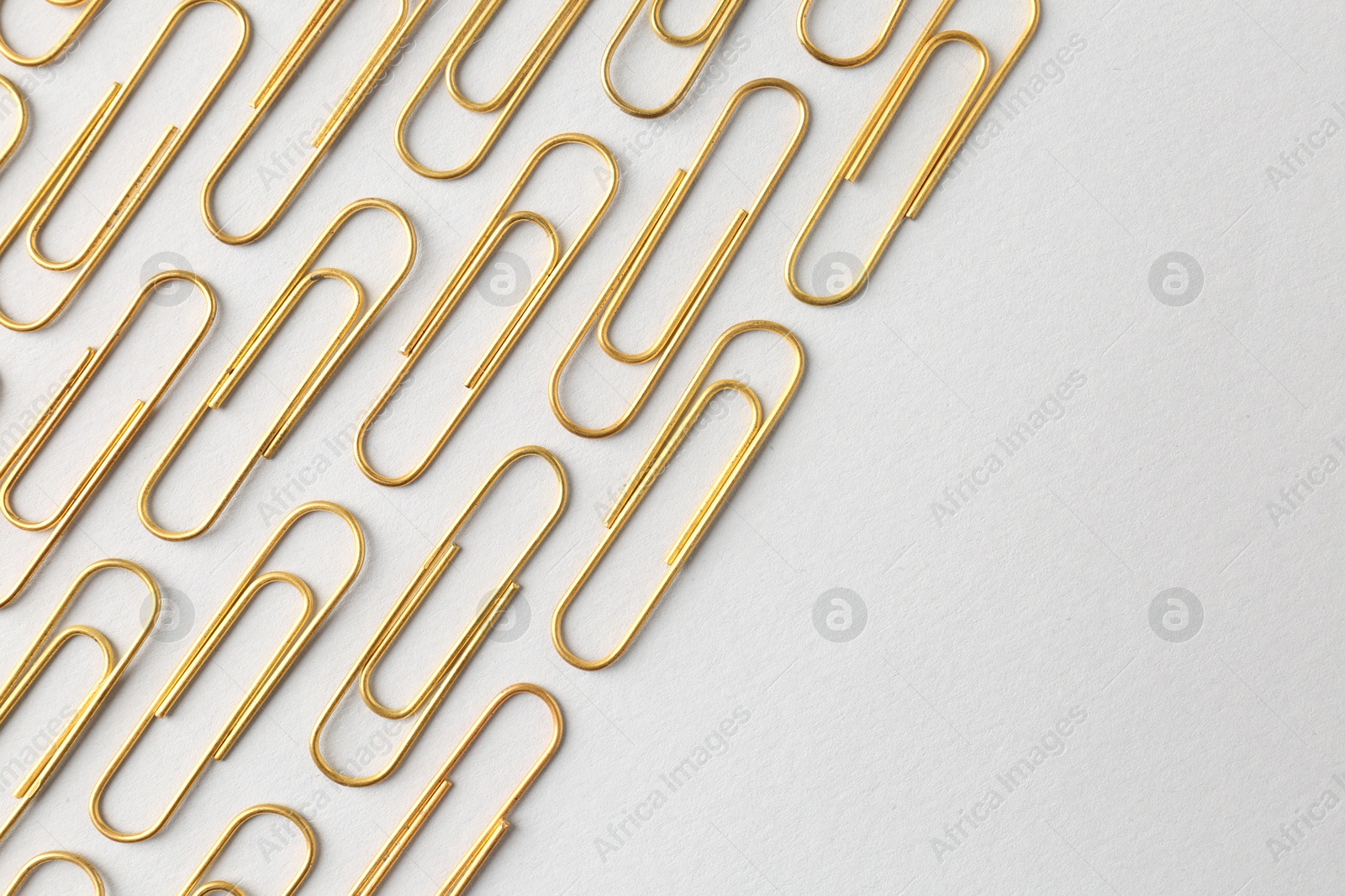 Photo of Golden paper clips on light background, flat lay. Space for text