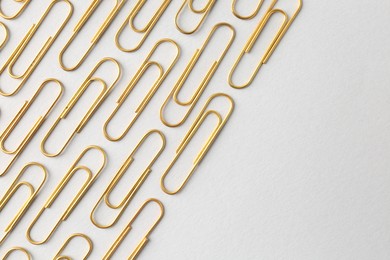 Photo of Golden paper clips on light background, flat lay. Space for text