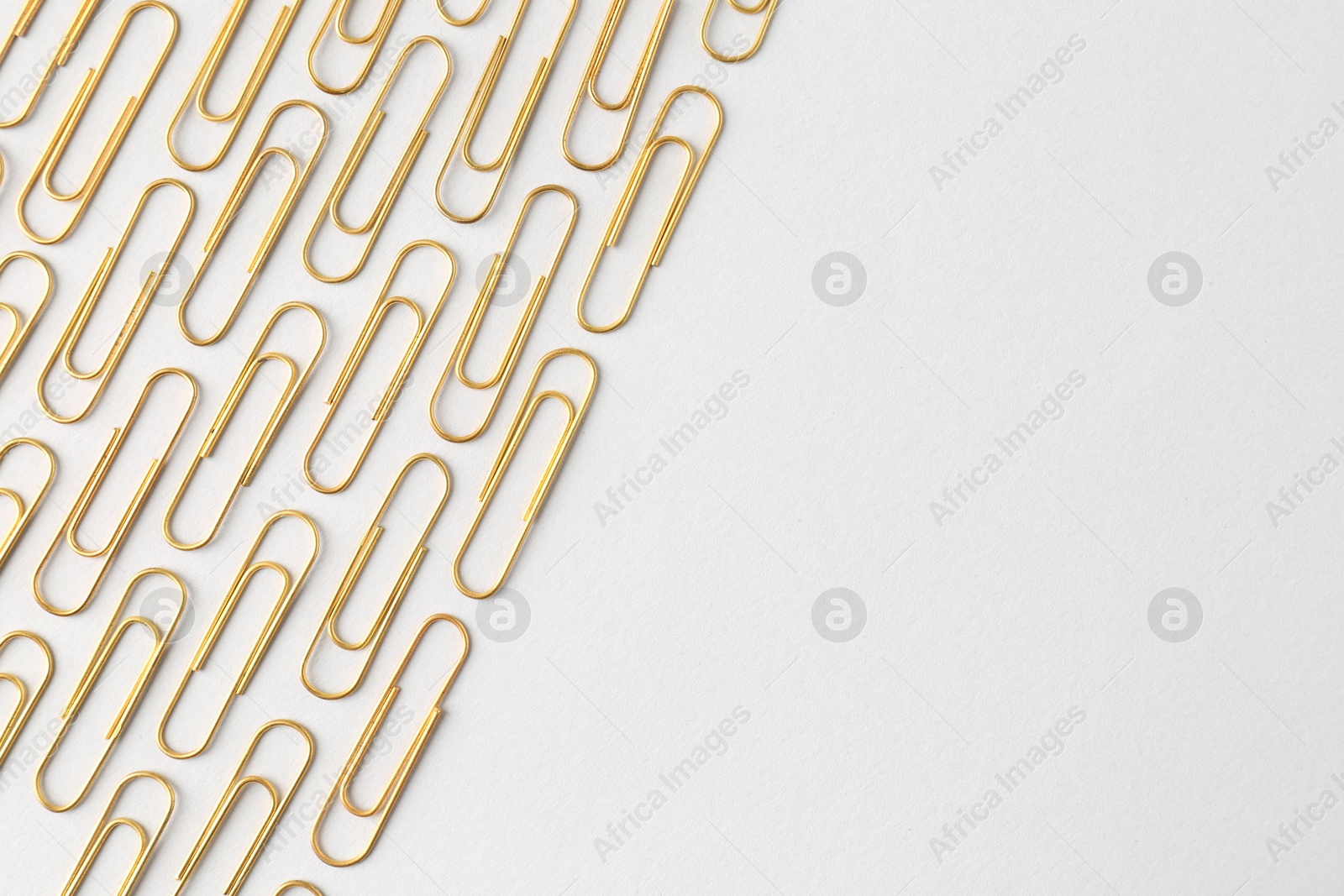 Photo of Golden paper clips on light background, flat lay. Space for text