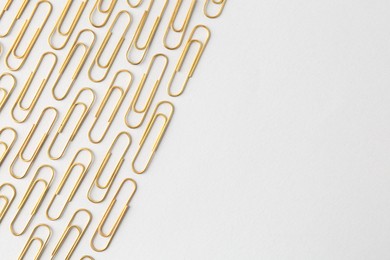 Photo of Golden paper clips on light background, flat lay. Space for text