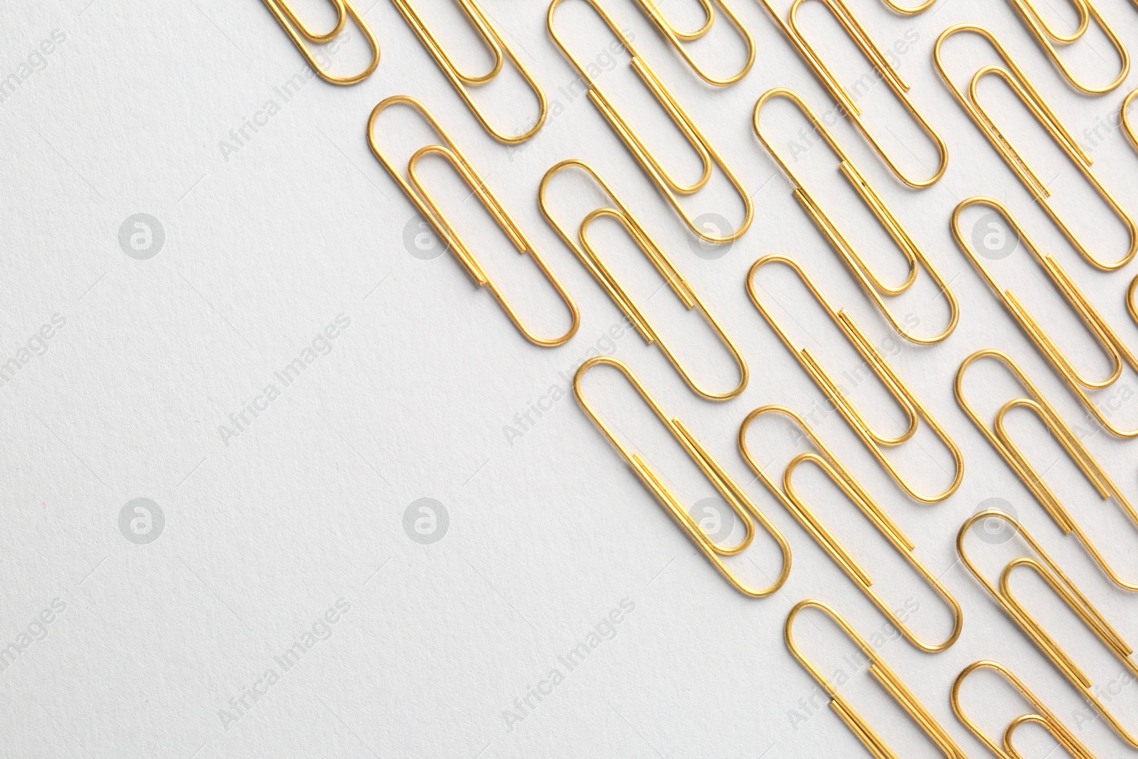 Photo of Golden paper clips on light background, flat lay. Space for text