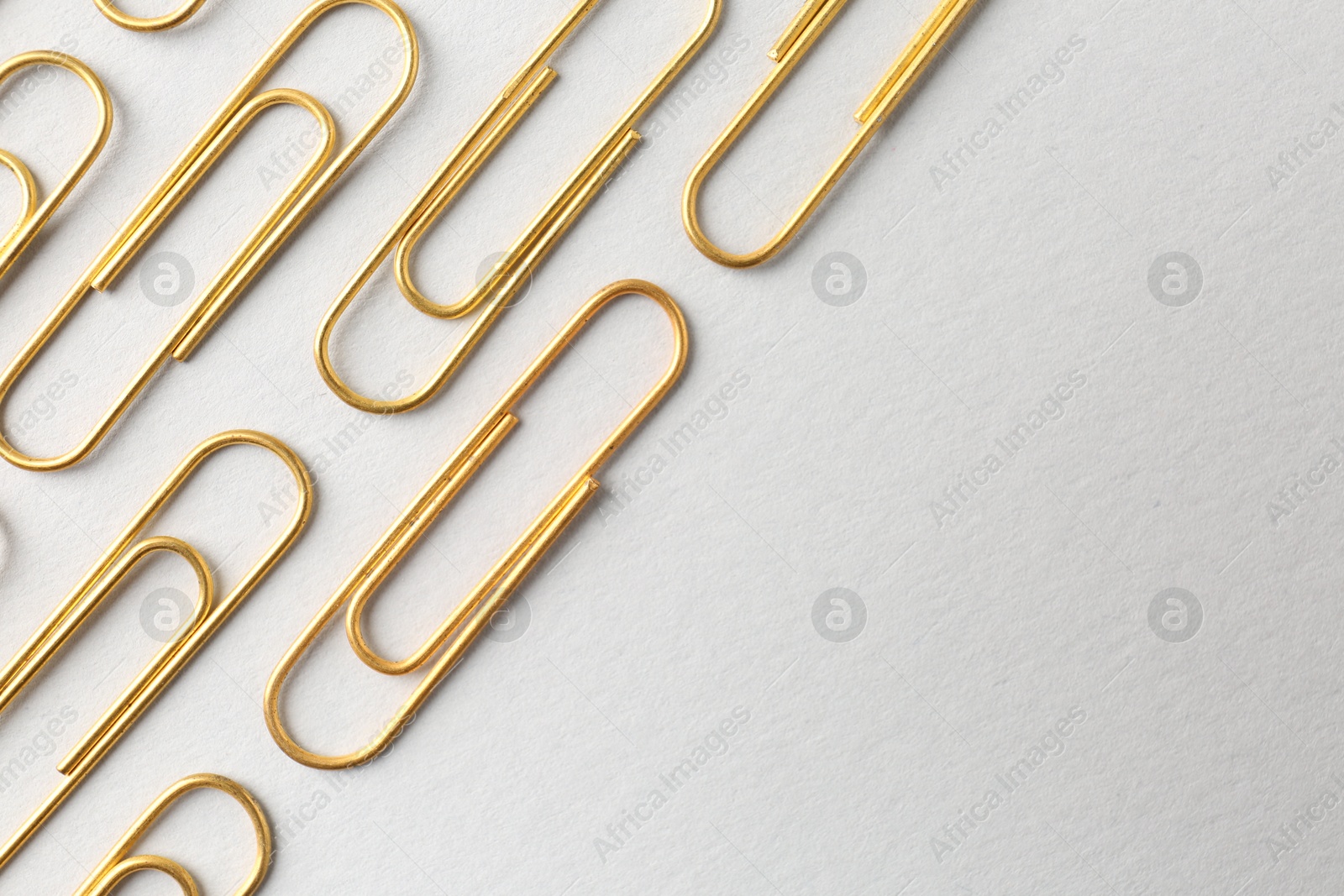 Photo of Golden paper clips on light background, flat lay. Space for text