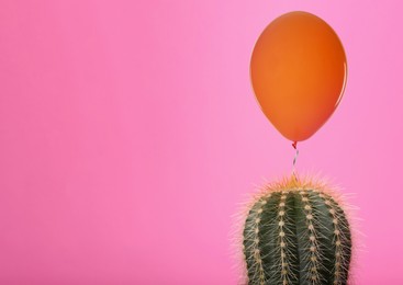 Image of Orange balloon and prickly cactus on pink background, space for text