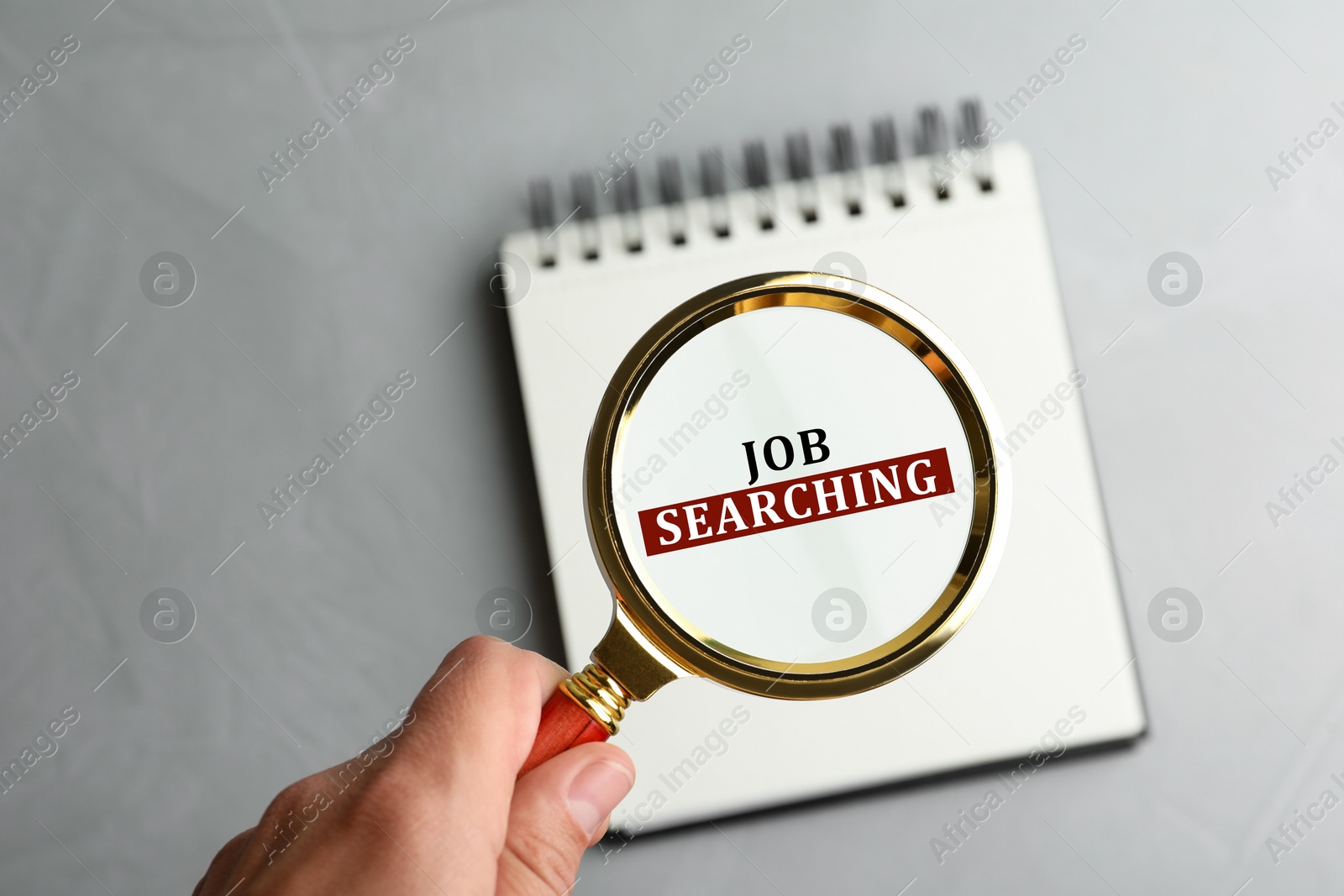 Image of Job search concept. Woman looking at words in notebook through magnifying glass on grey table, closeup