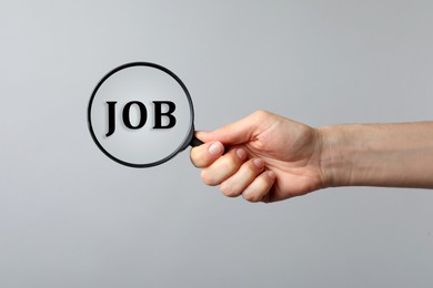 Image of Job search concept. Woman looking at word through magnifying glass on grey background, closeup