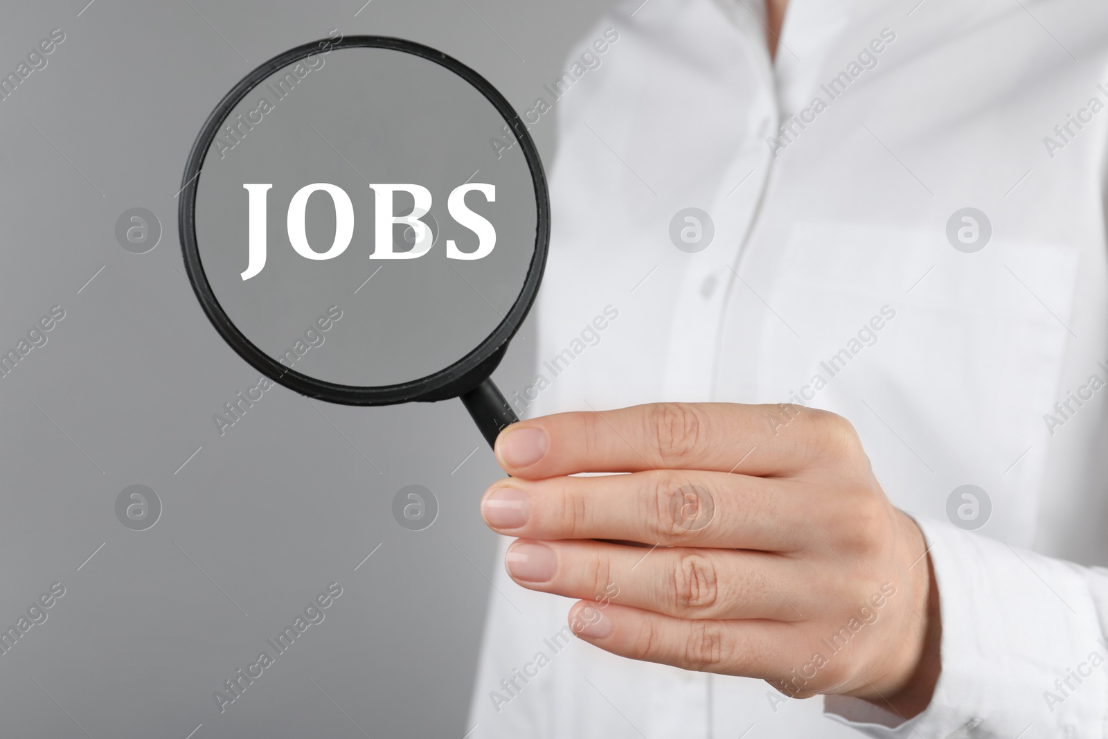 Image of Job search concept. Woman looking at word through magnifying glass on grey background, closeup