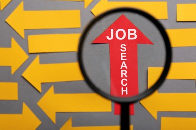 Image of Job search concept. Red paper arrow with words among orange ones on grey background, view through magnifying glass