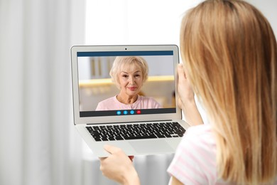 Grandmother and granddaughter talking via video call on laptop. Woman using computer at home