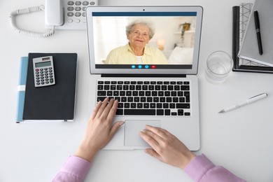 Image of Grandmother and granddaughter talking via video call on laptop. Woman using computer at table, top view