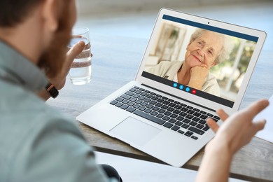 Grandmother and grandson talking via video call on laptop. Man using computer at table, closeup