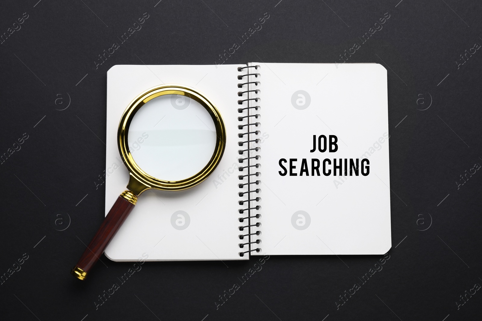 Image of Job search concept. Notebook with words and magnifying glass on black background, top view