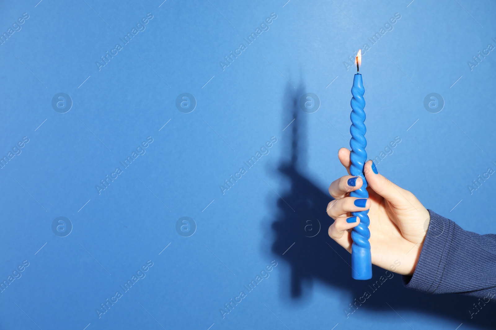 Photo of Woman holding burning candle on blue background, closeup. Space for text