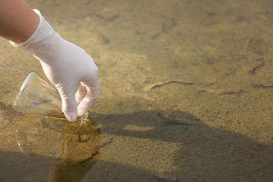 Photo of Examination of water quality. Researcher taking water sample from lake outdoors, closeup. Space for text