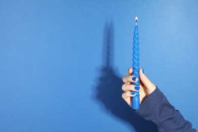 Photo of Woman holding burning candle on blue background, closeup. Space for text