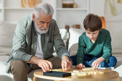 Photo of Grandpa and his grandson playing dominoes at table indoors