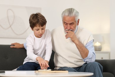 Photo of Grandpa and his grandson playing checkers at table indoors