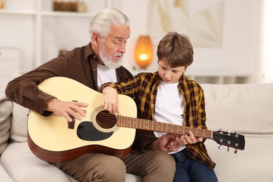 Photo of Grandpa teaching his grandson to play guitar on sofa at home