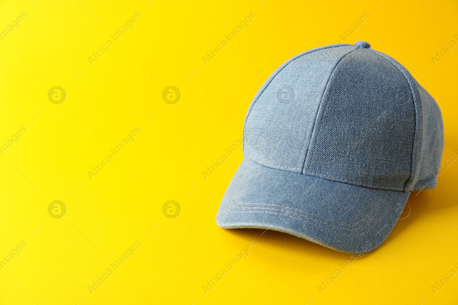 Photo of Stylish denim baseball cap on yellow background. Mockup for design