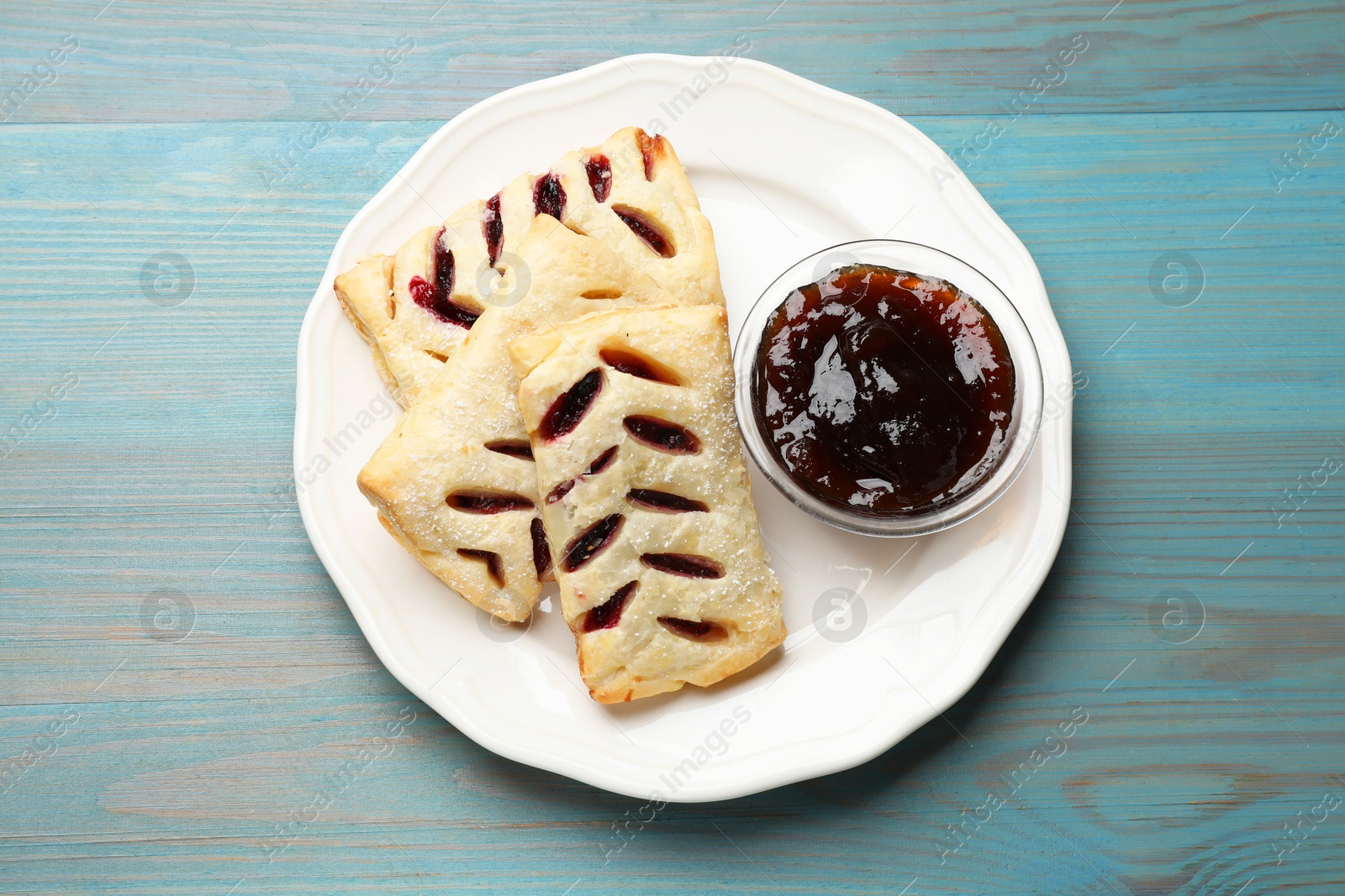 Photo of Delicious puff pastries and jam on light blue wooden table, top view