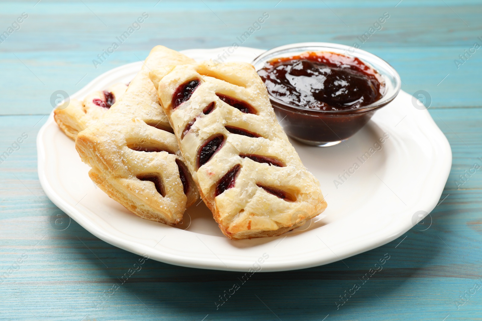 Photo of Delicious puff pastries and jam on light blue wooden table, closeup