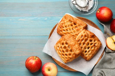 Photo of Delicious puff pastries, apples and powdered sugar on light blue wooden table, top view. Space for text