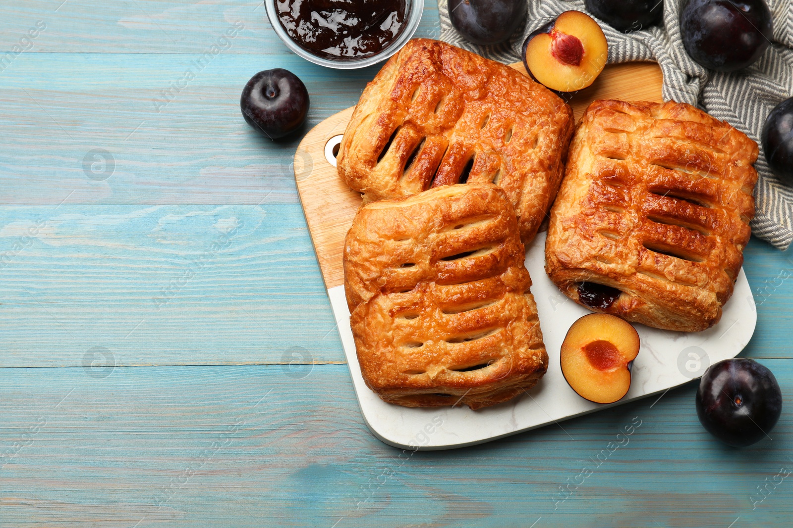 Photo of Delicious puff pastries, jam and plums on light blue wooden table, top view. Space for text