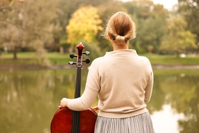 Photo of Woman with cello in park, back view. Classic musical instrument