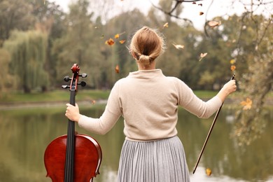 Woman with cello in park, back view. Classic musical instrument