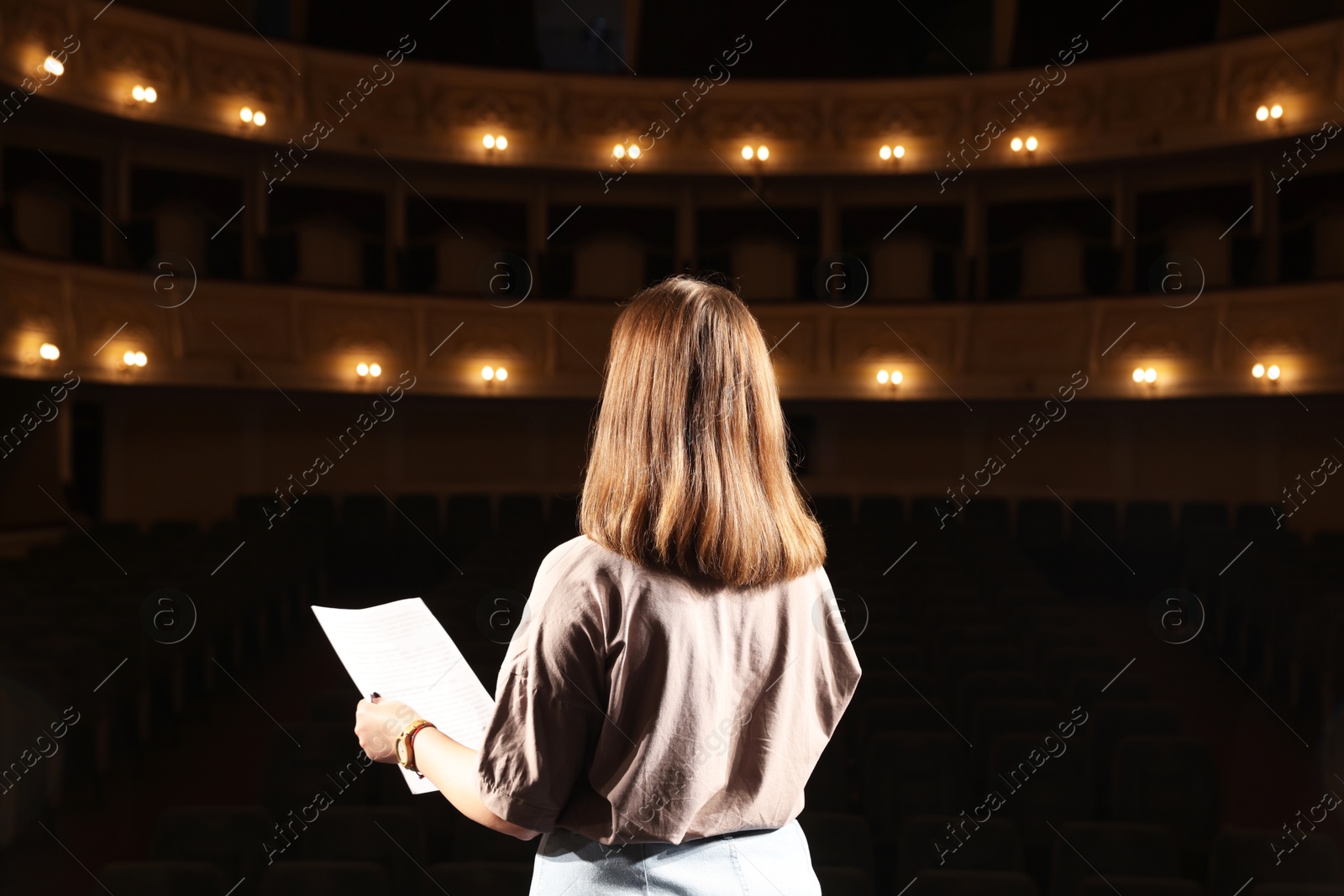 Photo of Professional actress rehearsing on stage in theatre, back view