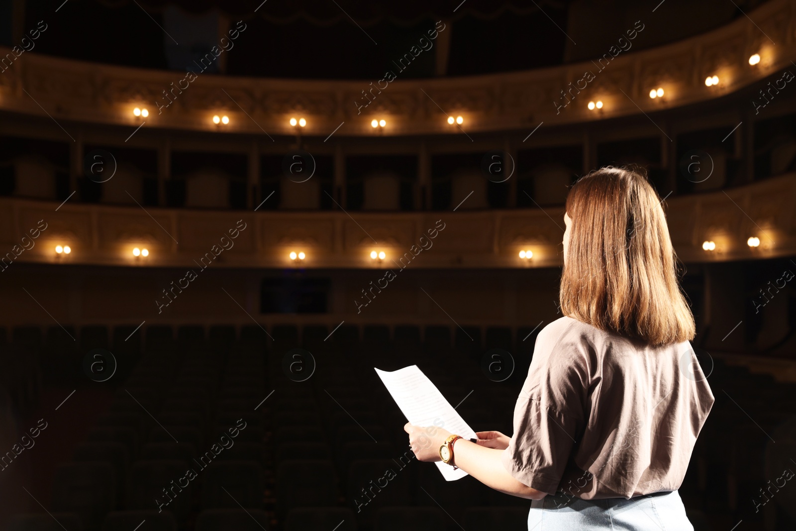 Photo of Professional actress rehearsing on stage in theatre, back view