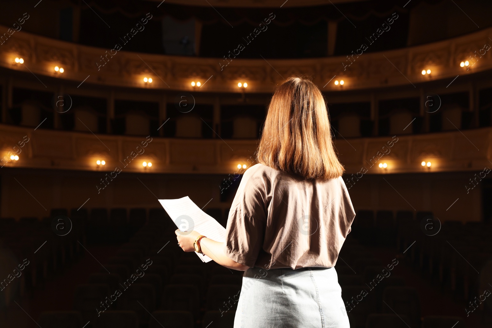 Photo of Professional actress rehearsing on stage in theatre, back view