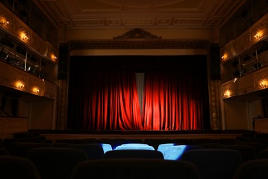 Photo of Elegant closed red curtains illuminated by spotlight in theatre