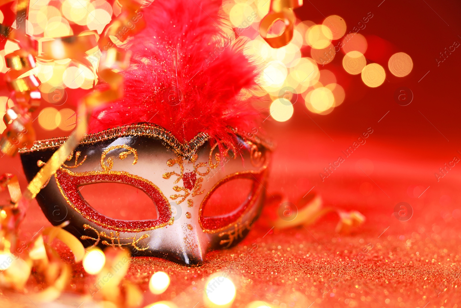 Photo of Beautiful carnival mask on shiny red background, closeup. Bokeh effect