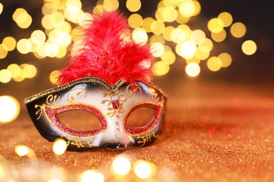 Photo of Beautiful carnival mask on shiny color background, closeup. Bokeh effect