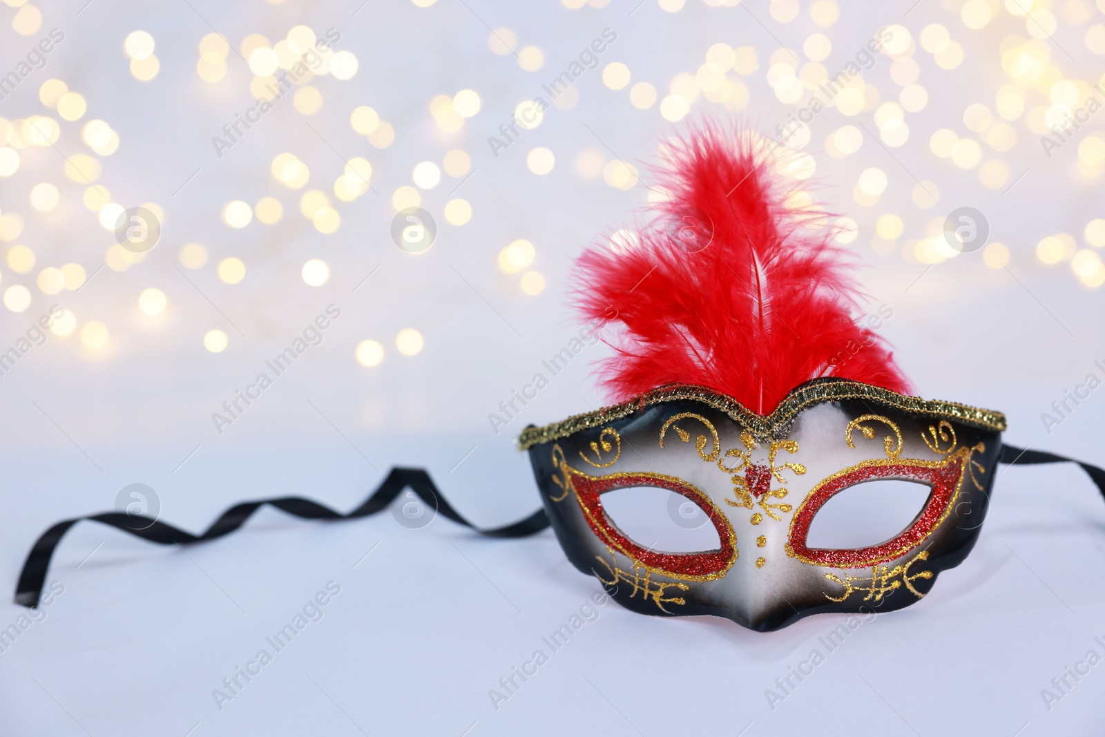 Photo of Beautiful carnival mask on color background, bokeh effect. Space for text