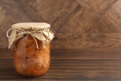 Photo of Canned meat in glass jar on wooden table, space for text