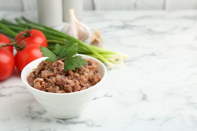 Photo of Canned meat in bowl, parsley, tomatoes and green onions on white marble table, closeup. Space for text