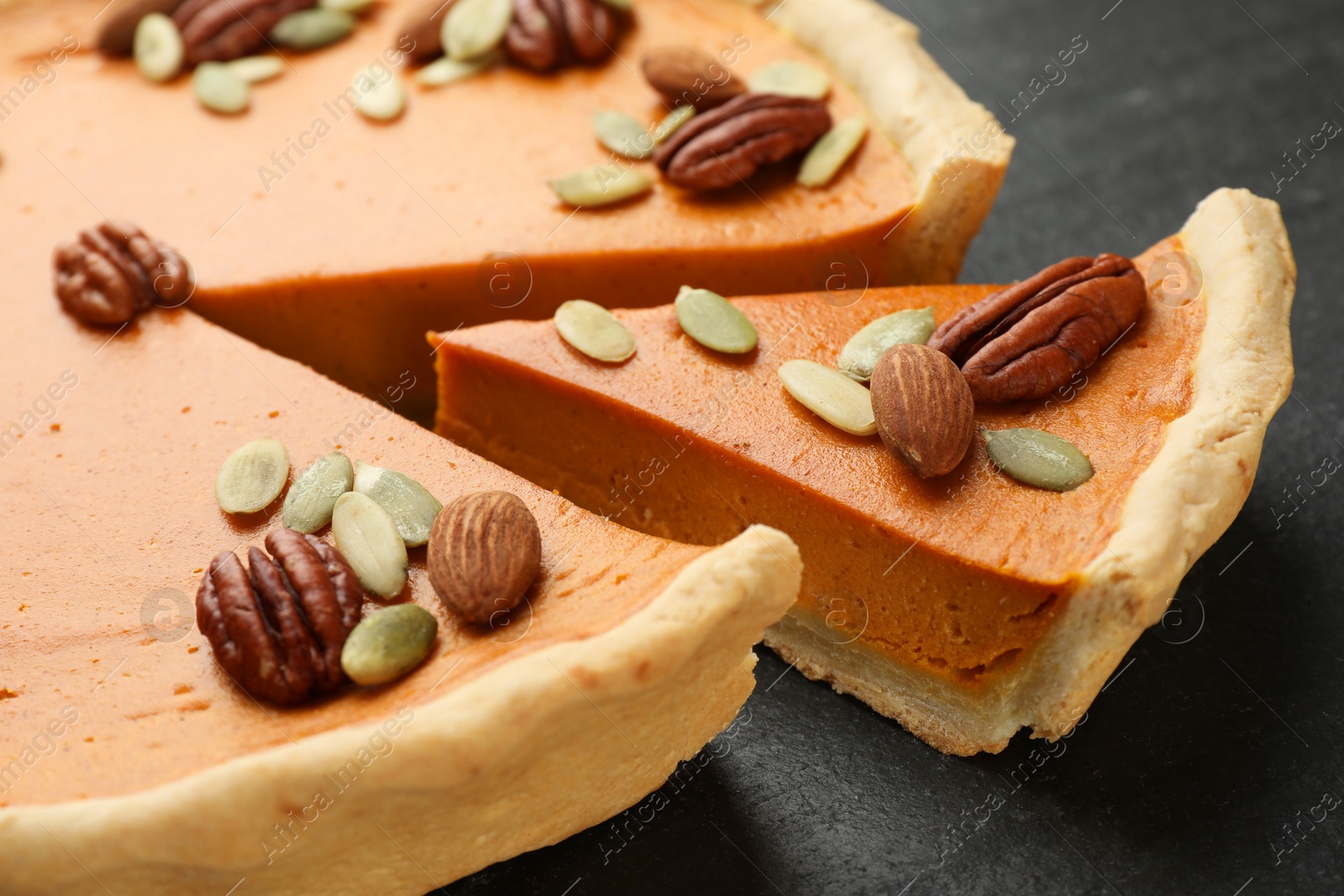 Photo of Pieces of tasty homemade pumpkin pie with seeds and nuts on black table, closeup