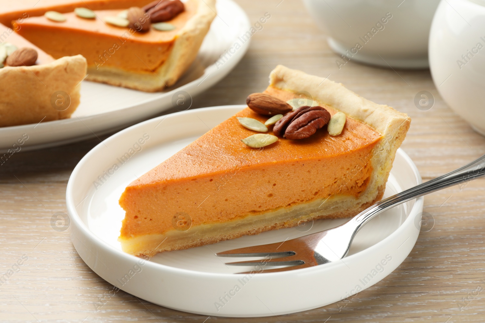 Photo of Piece of tasty homemade pumpkin pie with seeds and nuts on wooden table, closeup