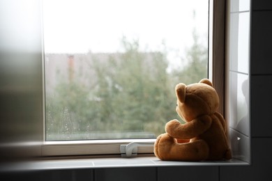 Photo of Lonely teddy bear near window on rainy day. Space for text