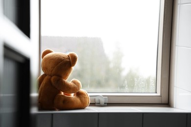 Photo of Lonely teddy bear near window on rainy day. Space for text