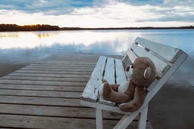 Photo of Lonely teddy bear on bench near river, space for text