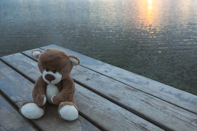 Photo of Lonely teddy bear on deck near river, space for text