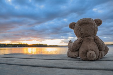 Photo of Lonely teddy bear on deck near river, back view. Space for text