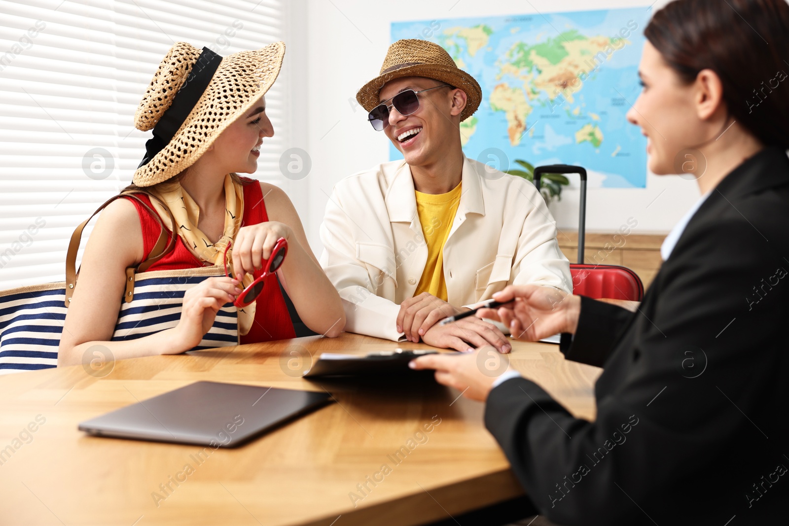 Photo of Happy couple planning vacation with travel agent at wooden table in office