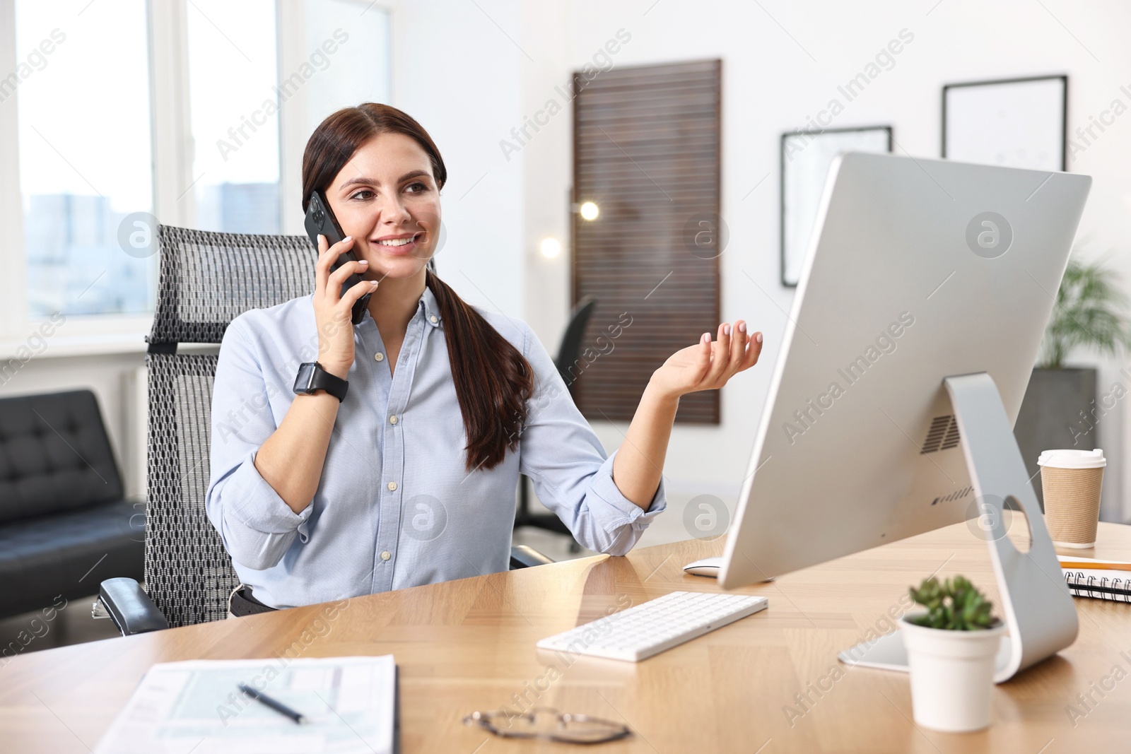 Photo of Woman talking on smartphone while working at table in office