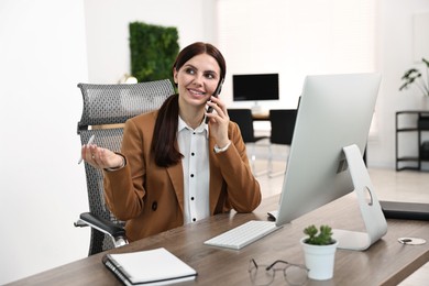 Photo of Woman talking on smartphone while working at table in office