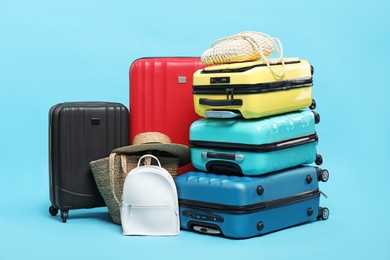 Photo of Colorful suitcases, backpack, beach bags and straw hat on light blue background