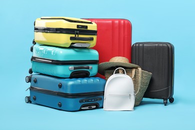 Photo of Colorful suitcases, backpack, beach bag and straw hat on light blue background